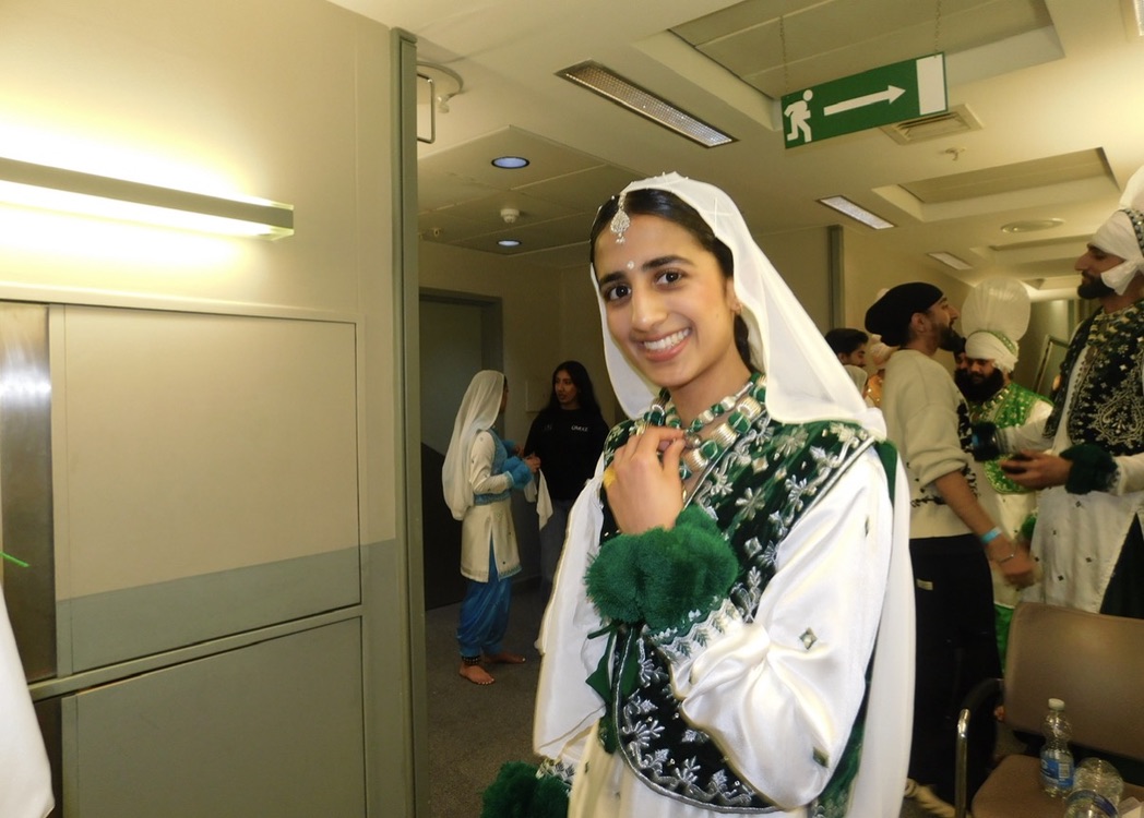 A LU Bhangra dancer in a green and white costume backstage